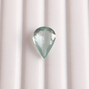Puede incluir: Una piedra preciosa de aguamarina en forma de l&aacute;grima de color azul claro.