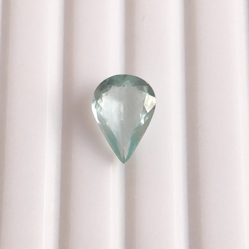 Puede incluir: Una piedra preciosa de aguamarina en forma de l&aacute;grima de color azul claro.