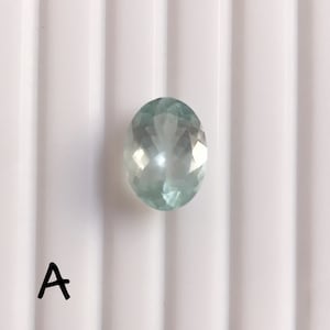 Puede incluir: Una piedra preciosa ovalada de color azul claro con facetas.