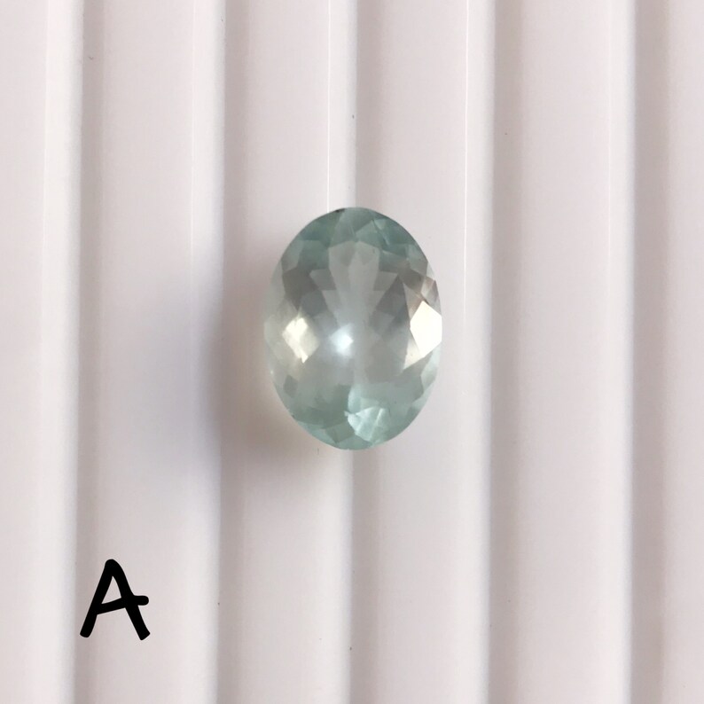 Puede incluir: Una piedra preciosa ovalada de color azul claro con facetas.
