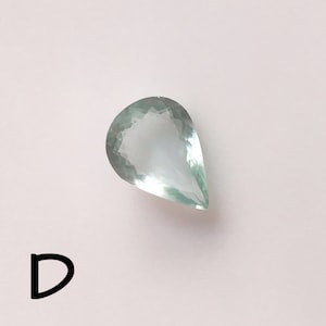 Puede incluir: Una piedra preciosa de color verde claro en forma de l&aacute;grima con un corte facetado.