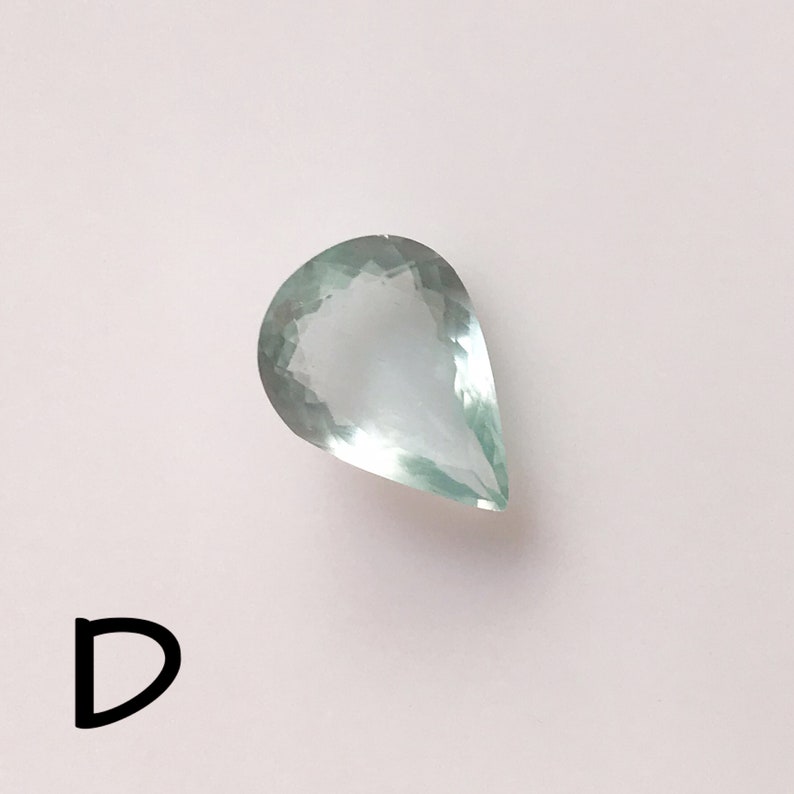 Puede incluir: Una piedra preciosa de color verde claro en forma de l&aacute;grima con un corte facetado.