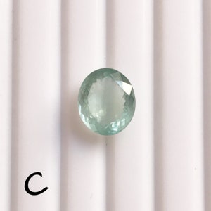 Puede incluir: Una piedra preciosa redonda de color verde claro con un corte facetado. La piedra preciosa est&aacute; sobre un fondo blanco.