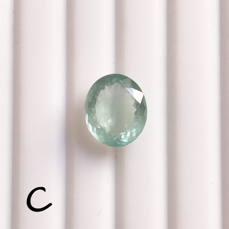 Puede incluir: Una piedra preciosa redonda de color verde claro con un corte facetado. La piedra preciosa est&aacute; sobre un fondo blanco.