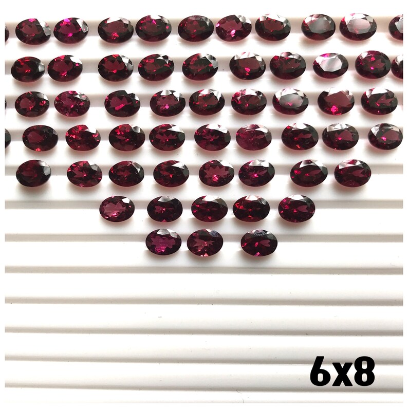 Puede incluir: Una colecci&oacute;n de 48 piedras preciosas ovaladas de color rojo oscuro dispuestas en forma de coraz&oacute;n sobre una superficie blanca. El texto "6x8" est&aacute; impreso en negro en la parte inferior de la imagen.