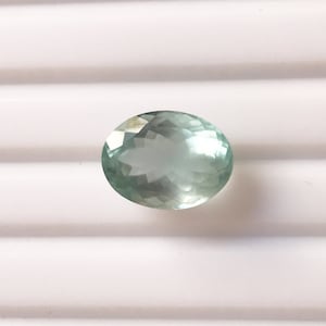 Puede incluir: Una piedra preciosa ovalada de color azul claro con un corte facetado.