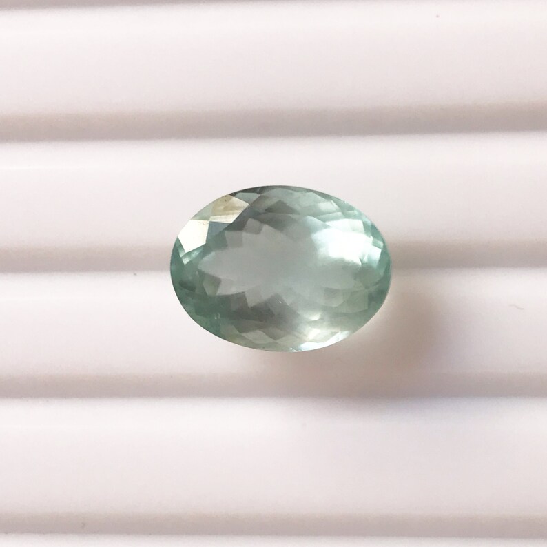 Puede incluir: Una piedra preciosa ovalada de color azul claro con un corte facetado.