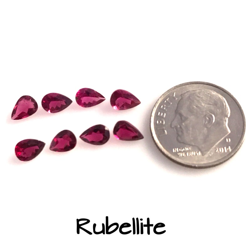 May include: Ten pear-shaped rubellite gemstones, each approximately the size of a ten pence coin, are arranged in two rows on a white surface. The gemstones are a deep pink colour and have a slight sparkle. A UK ten pence coin is included for size comparison.