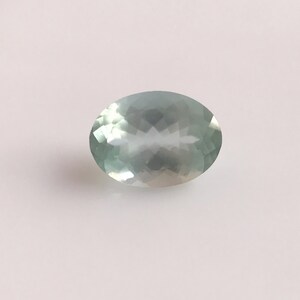 Puede incluir: Una piedra preciosa ovalada de color azul claro con un corte facetado.