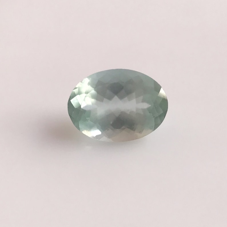 Puede incluir: Una piedra preciosa ovalada de color azul claro con un corte facetado.