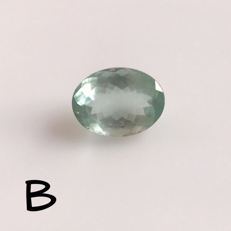 Puede incluir: Una piedra preciosa ovalada de color verde claro con un corte facetado.