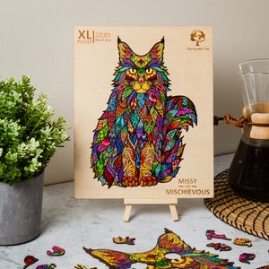 May include: A 330-piece XL jigsaw puzzle featuring a colorful, intricate design of a Maine Coon cat. The puzzle is made of wood and is titled "Missy the Mischievous".
