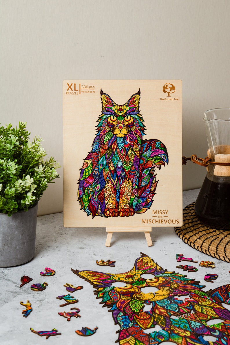 May include: A 330-piece XL jigsaw puzzle featuring a colorful, intricate design of a Maine Coon cat. The puzzle is made of wood and is titled "Missy the Mischievous".