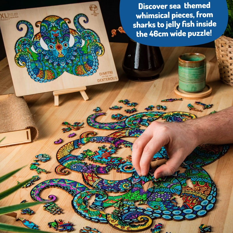 May include: A colorful wooden jigsaw puzzle of an octopus with intricate details. The puzzle is partially assembled on a wooden table with a few pieces scattered around. The completed puzzle is shown on a wooden easel with the text "DIMITRI DEXTEROUS" and "XL 121" printed on it. The text "Discover sea themed whimsical pieces, from sharks to jelly fish inside the 46cm wide puzzle!" is printed on a white background.