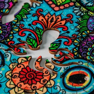 May include: A colorful wooden jigsaw puzzle with a skull design. The puzzle pieces are intricately cut and feature a variety of floral patterns in shades of blue, green, red, and yellow.