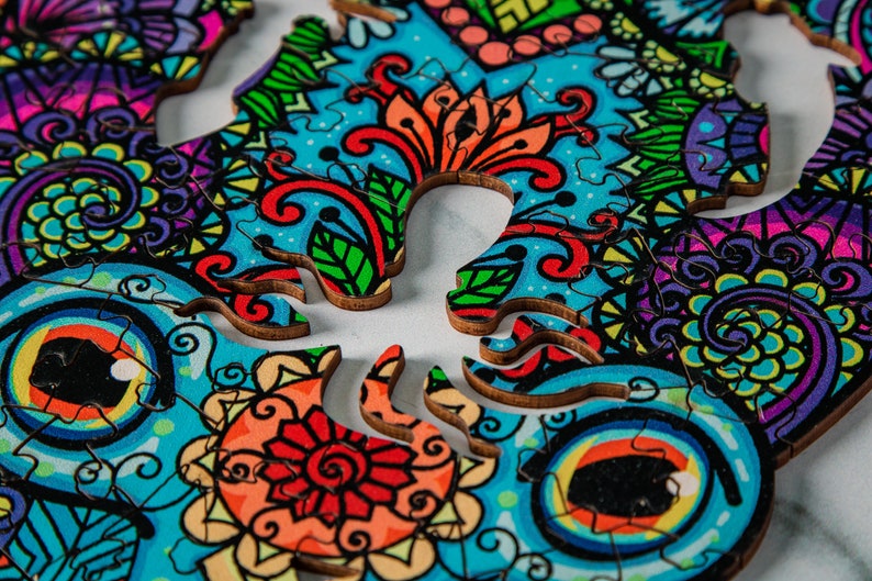 May include: A colorful wooden jigsaw puzzle with a skull design. The puzzle pieces are intricately cut and feature a variety of floral patterns in shades of blue, green, red, and yellow.