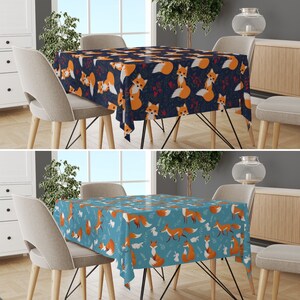 May include: Two square dining tables with different coloured tablecloths. The tablecloth on the left table is dark blue with a pattern of orange foxes and red berries. The tablecloth on the right table is light blue with a pattern of orange foxes and white rabbits. Both tables have a metal frame.