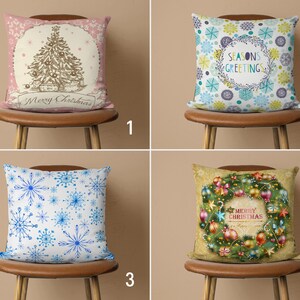 May include: Four different Christmas cushion designs. The first cushion is pink with a brown Christmas tree and the text "Merry Christmas". The second cushion is blue with a wreath and the text "Seasons Greetings". The third cushion is white with a blue snowflake pattern. The fourth cushion is beige with a green wreath and the text "Merry Christmas".