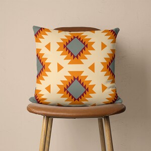 Op de afbeelding: Een decoratief kussen met een geometrisch patroon in tinten oranje, bordeauxrood en grijs. Het kussen ligt op een bruine leren stoel.
