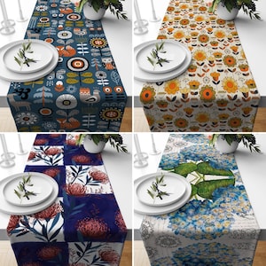 May include: Four different table runners with various patterns. The first runner has a blue background with white, red, and yellow geometric shapes and a fox design. The second runner has a beige background with yellow, orange, and brown floral designs. The third runner has a blue and white checkered background with red and pink floral designs. The fourth runner has a white background with blue and green floral designs and a handwritten text.