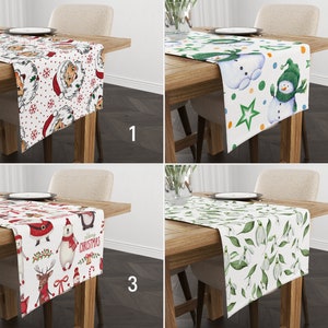 May include: Four different Christmas table runners with various designs. The first runner features a white background with red and green Santa Claus faces. The second runner has a white background with green and blue snowmen. The third runner has a white background with red and green Christmas characters. The fourth runner has a white background with green leaves and white flowers.