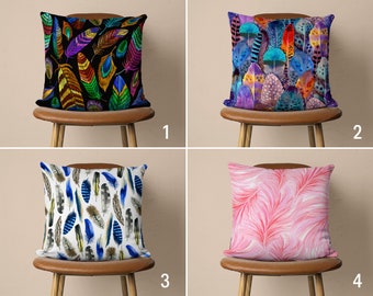 May include: Four decorative throw pillows with different feather patterns. The pillows are on brown chairs with wooden legs. The pillows are in the following order: 1) multi-colored feathers on a black background, 2) multi-colored feathers on a purple background, 3) blue and white feathers on a white background, 4) pink feathers on a pink background.