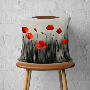 Puede incluir: Una almohada blanca con un dise&ntilde;o de flores de amapola roja. La almohada presenta un campo de tallos de amapola negros y blancos con flores de amapola rojas.