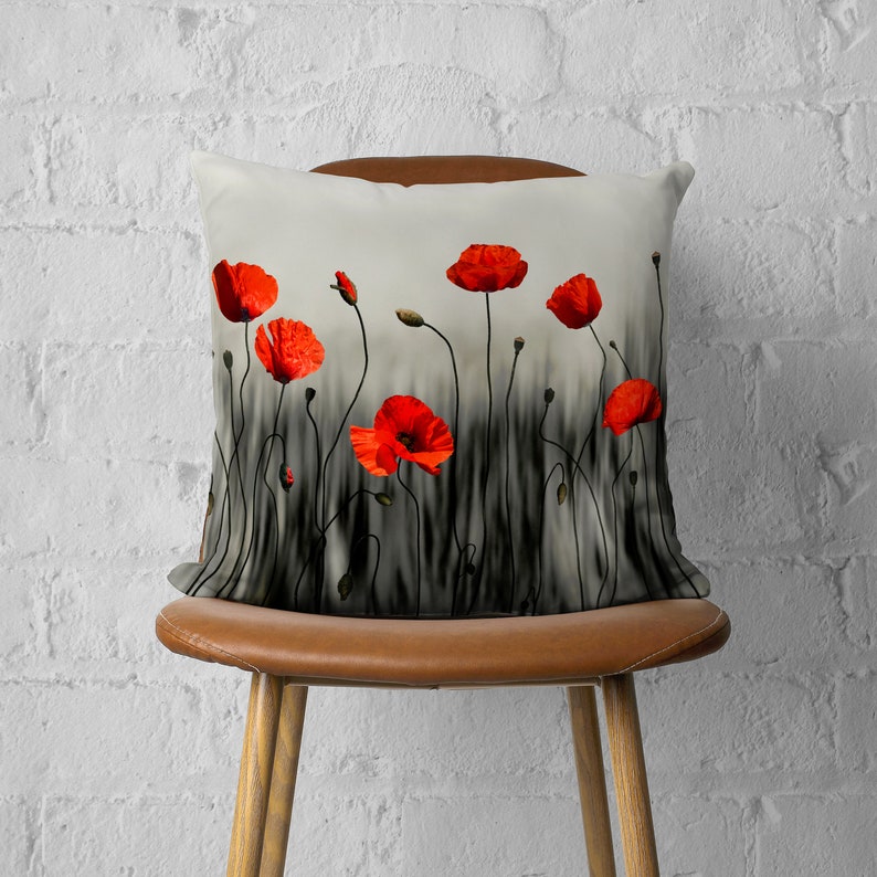 Puede incluir: Una almohada blanca con un dise&ntilde;o de flores de amapola roja. La almohada presenta un campo de tallos de amapola negros y blancos con flores de amapola rojas.
