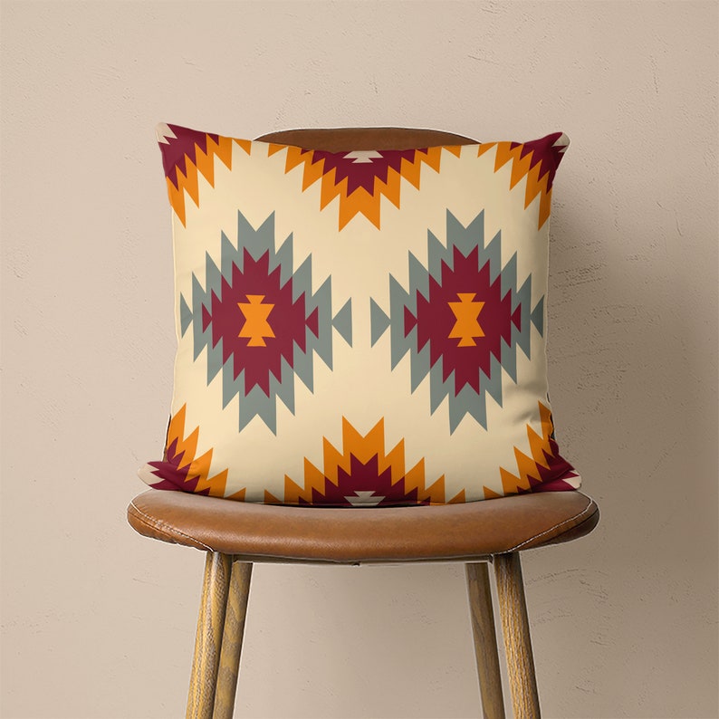 Op de afbeelding: Een decoratief kussen met een geometrisch patroon in tinten oranje, rood, grijs en beige. Het kussen ligt op een bruine stoel.