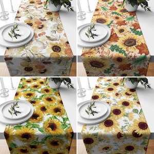 May include: Four different table runners with sunflower designs. The runners are all white with a floral pattern and feature sunflowers in various shades of yellow, orange, and brown. The runners are all 14 inches wide and 70 inches long.