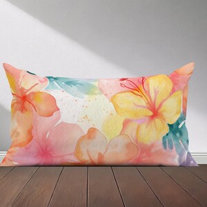 Peut inclure: Un coussin rectangulaire avec un motif floral aquarelle. Le coussin pr&eacute;sente des fleurs roses, jaunes et vertes sur un fond blanc.