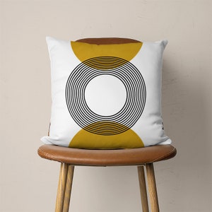 May include: White throw pillow with a black and yellow geometric design. The design features a circle with concentric rings and two half circles on either side.