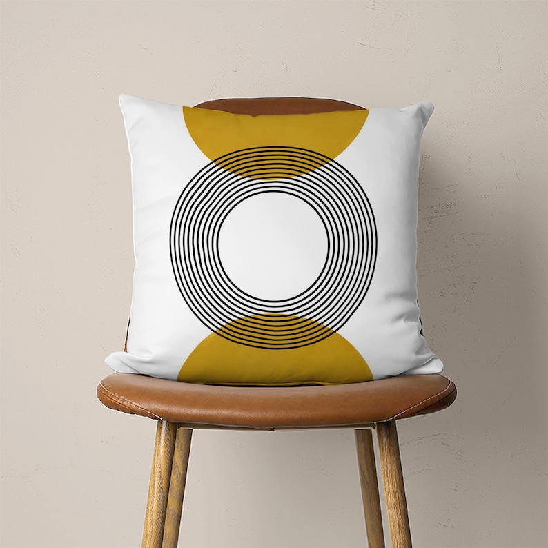 May include: White throw pillow with a black and yellow geometric design. The design features a circle with concentric rings and two half circles on either side.