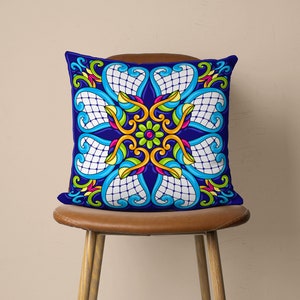 May include: A blue cushion with a colourful, intricate floral design. The cushion features a repeating pattern of flowers, leaves, and swirls in shades of yellow, green, pink, and blue.