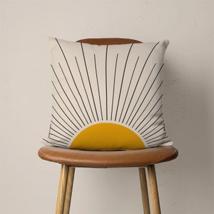 May include: A white throw pillow with a black and yellow sunburst design. The pillow is sitting on a brown leather chair.