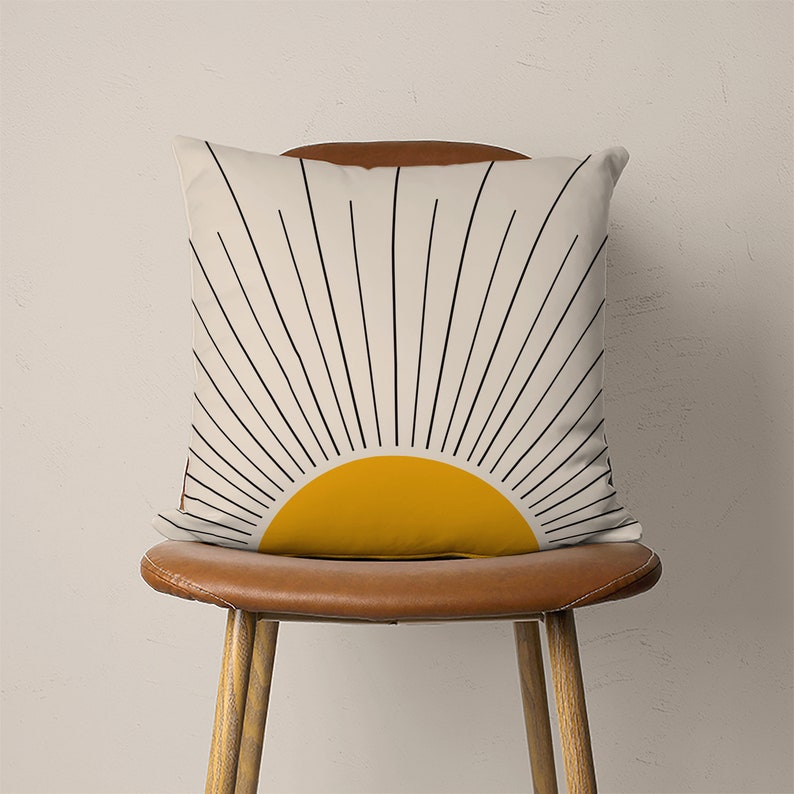 May include: A white throw pillow with a black and yellow sunburst design. The pillow is sitting on a brown leather chair.