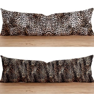 Puede incluir: Dos almohadas rectangulares largas con un estampado de leopardo. La almohada superior tiene un fondo más claro con manchas marrones y negras. La almohada inferior tiene un fondo más oscuro con manchas marrones y negras.