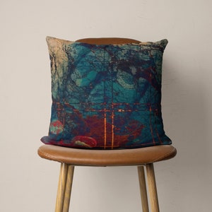 May include: A teal, red, and orange abstract patterned throw pillow on a brown leather chair.