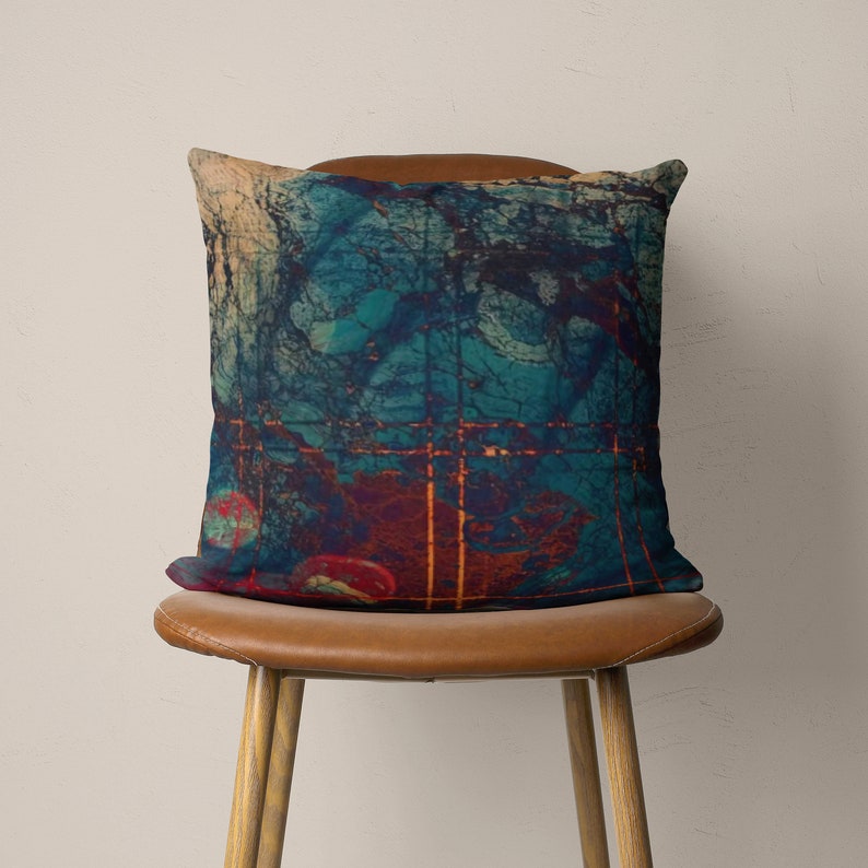 May include: A teal, red, and orange abstract patterned throw pillow on a brown leather chair.