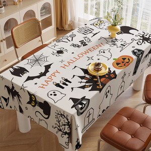 May include: White tablecloth with a black and orange Halloween theme. The tablecloth features a variety of Halloween icons, including ghosts, pumpkins, bats, spiders, and a haunted house. The text "Happy Halloween!" is printed in black letters on the tablecloth.