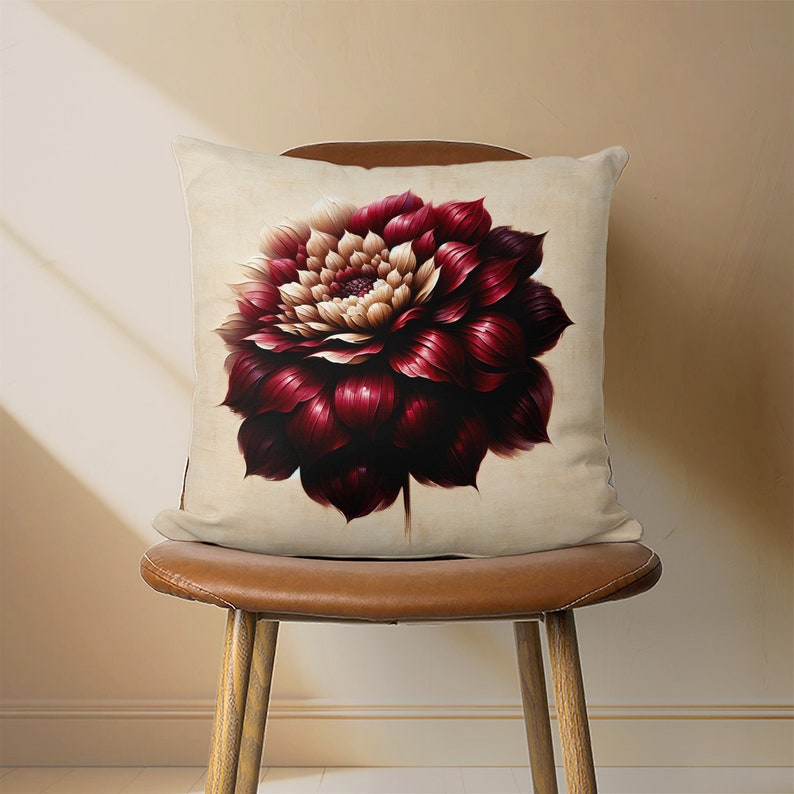 May include: A cream-colored pillow with a large, burgundy and cream-colored flower printed on it. The pillow is sitting on a brown leather chair.