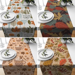May include: Four different table runners with autumn leaf designs. The runners are in various colours, including brown, orange, green, and beige. The designs feature leaves, berries, and other autumnal elements.