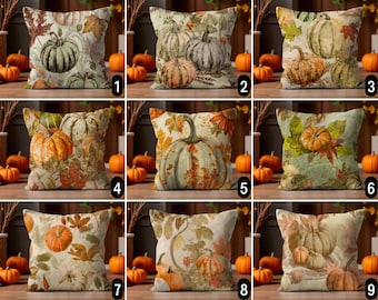 May include: Decorative throw pillows with autumn-themed pumpkin designs. Each pillow features a different pumpkin illustration, surrounded by fall leaves in shades of orange, green, and brown. The pillows are square-shaped and rest on a wooden surface.