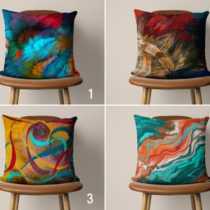 May include: Four decorative throw pillows with abstract designs. The pillows are on brown chairs with wooden legs. The pillows feature a variety of colours, including blue, red, yellow, orange, and green.