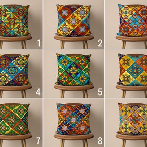 Puede incluir: Nueve fundas de cojín diferentes con coloridos patrones geométricos. Los patrones presentan una mezcla de colores rojo, amarillo, azul, verde y marrón. Los cojines se muestran en sillas marrones sobre un fondo blanco.