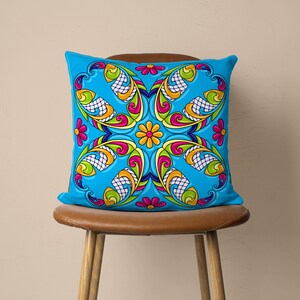 May include: A blue cushion with a colourful floral pattern. The pattern features bright pink, yellow, green, and orange colours. The cushion is sitting on a brown chair.