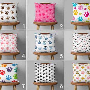 May include: Nine decorative throw pillows with paw print patterns. The pillows feature various color schemes, including brown, pink, blue, and black, with different paw print designs. Each pillow is displayed on a wooden stool.
