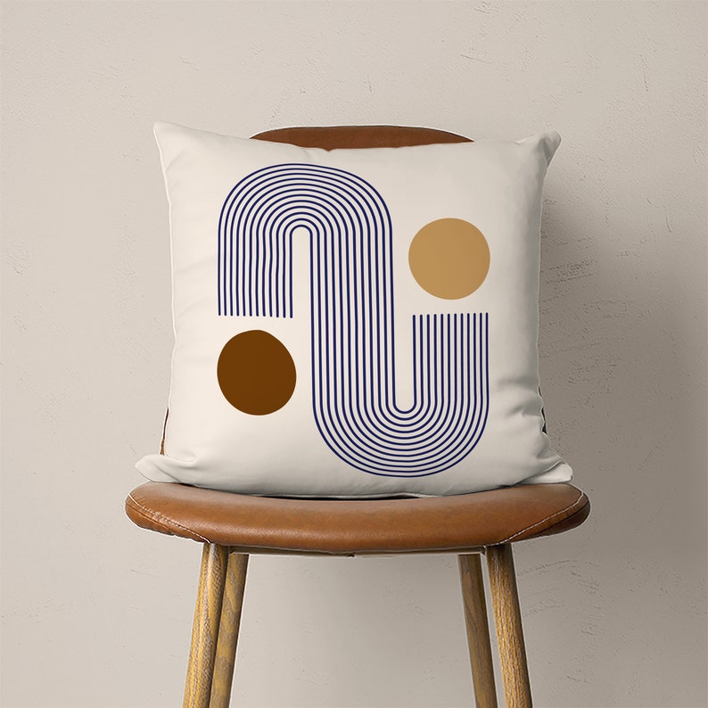May include: White throw pillow with a navy blue and brown abstract design. The design features a curved striped pattern with two circles.