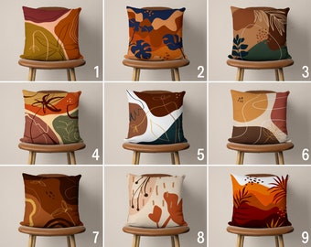 May include: Nine different throw pillow designs with abstract patterns in shades of brown, orange, green, and white. The pillows are arranged on chairs with brown wooden frames.