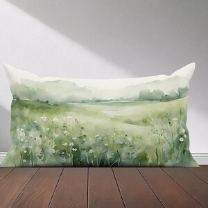 Peut inclure: Un oreiller en aquarelle vert et blanc repr&eacute;sentant une sc&egrave;ne de paysage avec un champ de fleurs et une cha&icirc;ne de montagnes au loin.